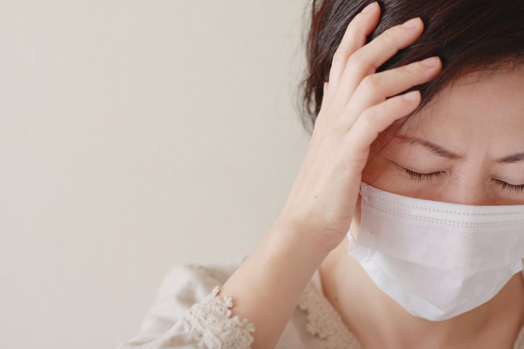 マスクをしてこめかみに手をあてる女性